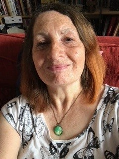 A person with shoulder length brown hair and wearing a blue and white butterfly top smiling in a selfie.