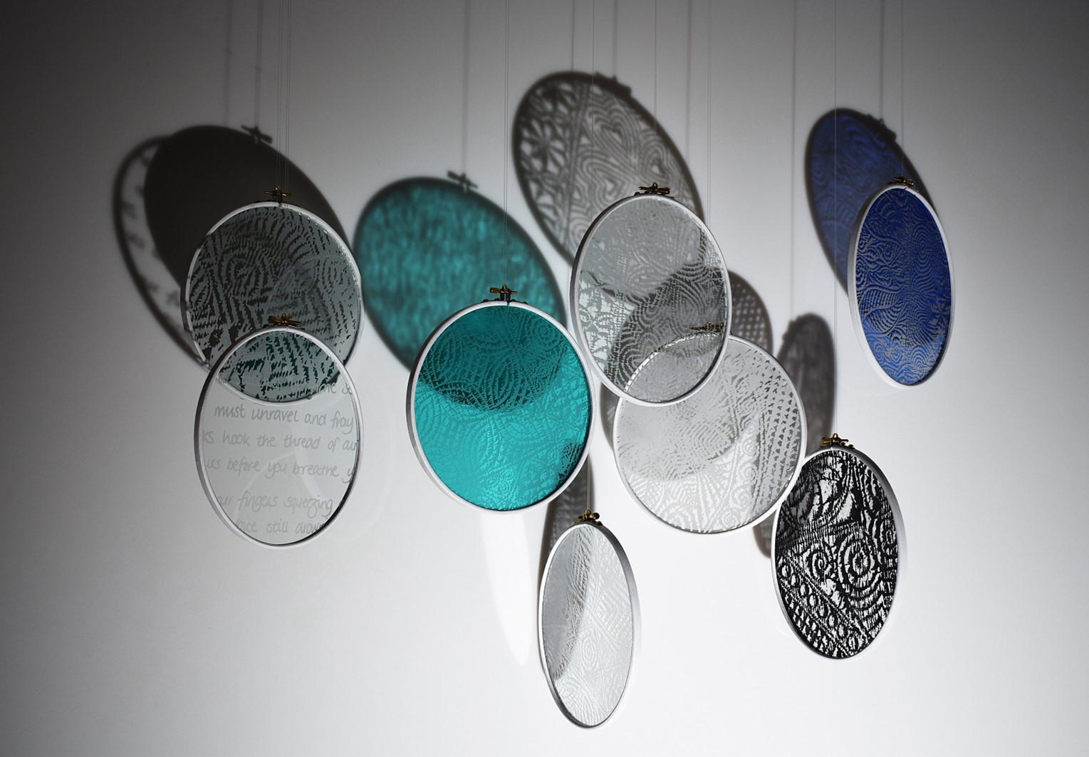 Image of glass circles hanging by threads framed in silver, some have colours others have writing