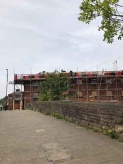 A view from a cobbled street of a brick building in the distance covered in scaffolding.